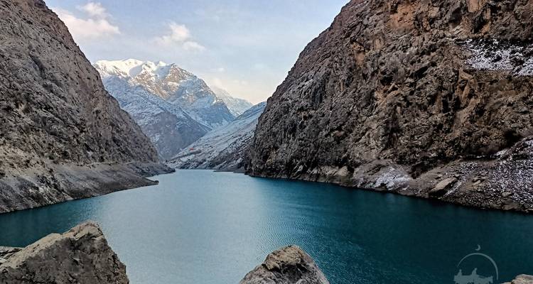 Turquoise mountain reservoir flanked by steep, snow-dusted cliffs.