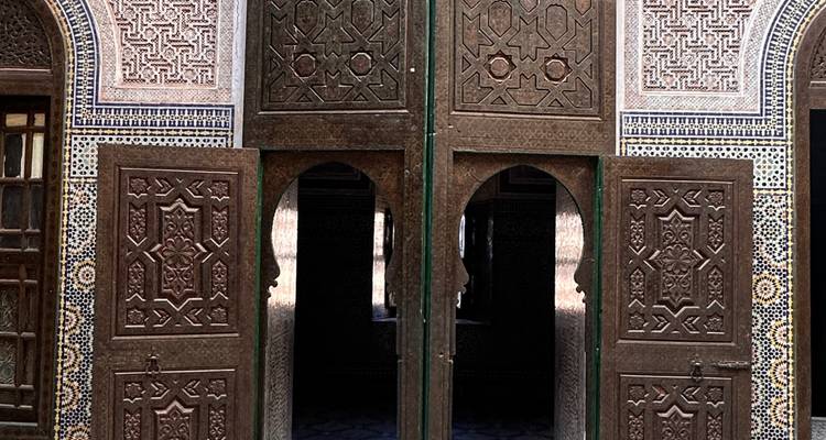 Puertas de madera talladas con intrincados detalles y azulejos zellige coloridos de una medersa marroquí.