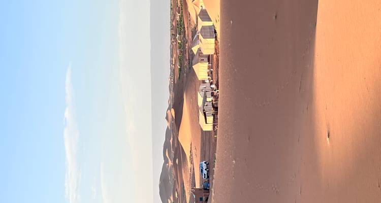 Fila de tiendas blancas de desierto dispersas entre dunas de arena ondulantes bajo una suave luz del atardecer.