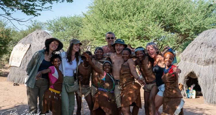 Travelers posing happily with San bushmen in front of grass huts