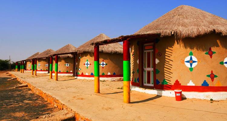 Row of traditional circular mud huts with colorful tribal paintings in bright sunlight