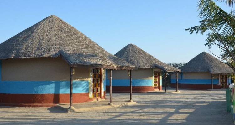 Simple thatched round huts painted with horizontal colored bands in a sandy courtyard