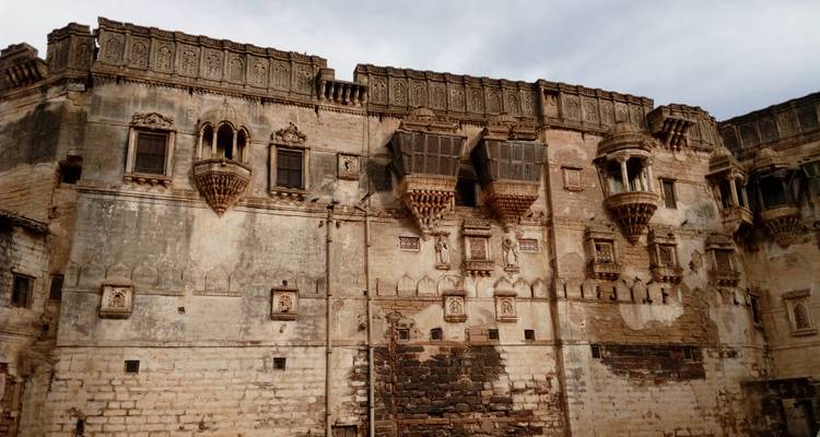Weathered façade of an ornate historic palace with intricate stone balconies and carvings