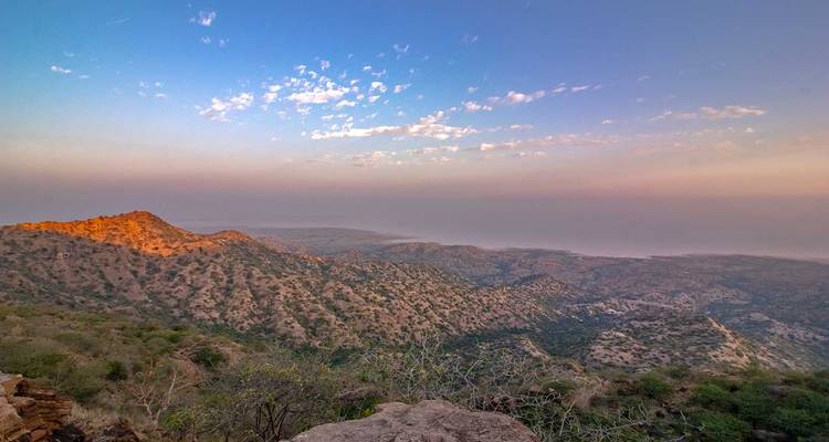 Expansive view of arid rolling hills and distant haze at sunrise casting warm light