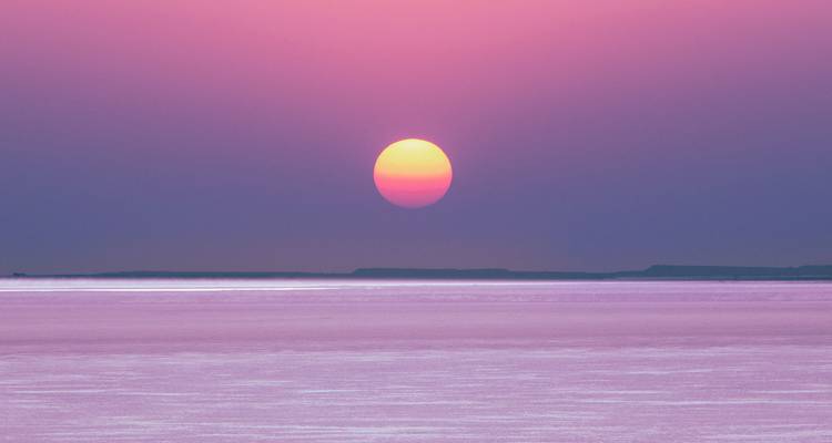 Vibrant pink and purple sunset over a calm salt desert horizon with the sun low above