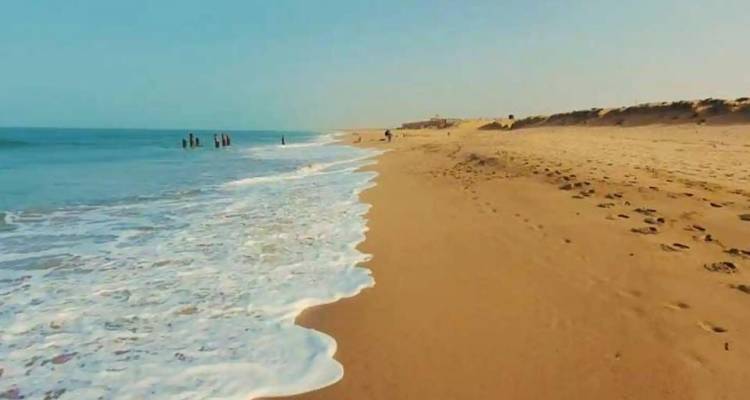 Sandy beach with gentle surf and distant swimmers on a clear day