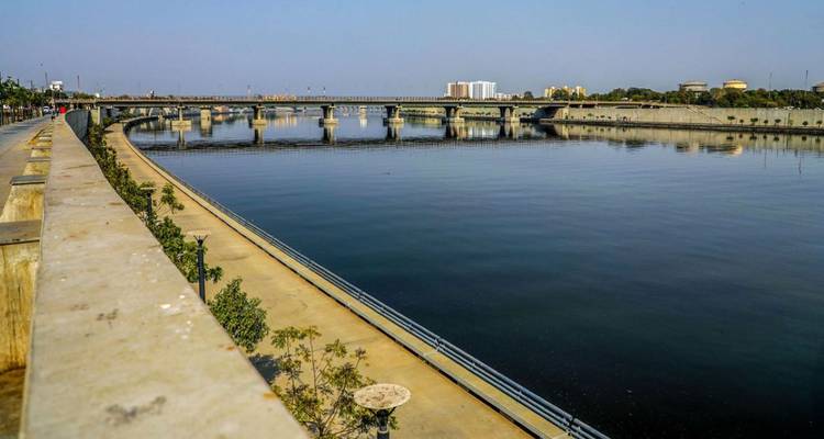 Urban riverfront promenade with curved bridge and calm reflective water under clear sky