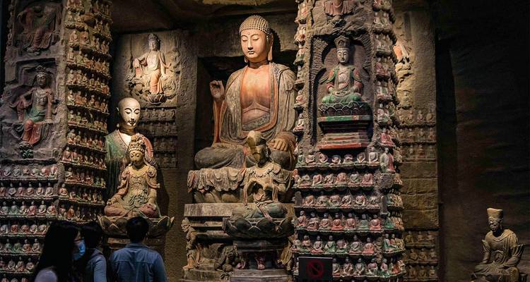 Visitors observe intricately carved Buddhist statues in a dimly lit cave temple