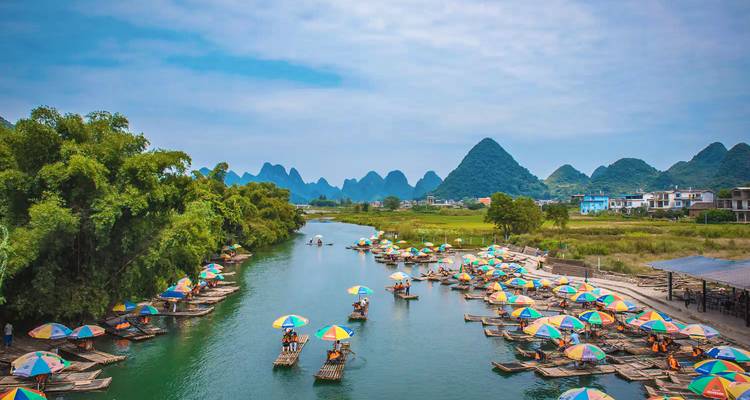 Dozens of bamboo rafts with colorful umbrellas float on a serene river amid karst mountains