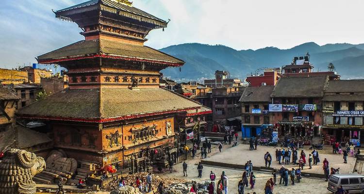 Traditionele pagode- en paleistructuren torenen uit boven het levendige plein van Bhaktapur met bergen als silhouet op de achtergrond.