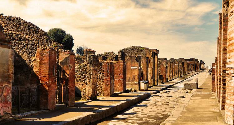 Sun-drenched ancient street ruins of Pompeii lined with brick columns and stone pavement.