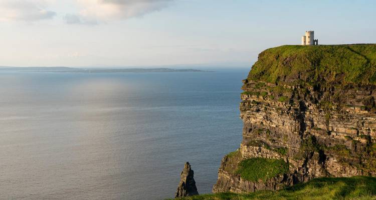 La Torre O'Brien se alza en lo alto de los verdes Acantilados de Moher con vistas a un tranquilo horizonte del Atlántico al atardecer
