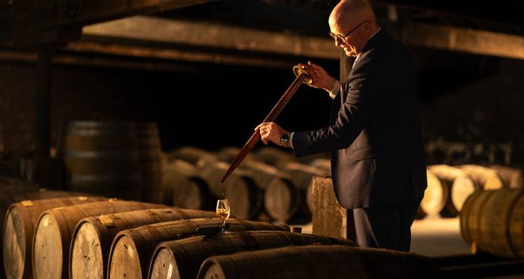 El maestro destilador extrae una muestra de barriles de whiskey envejecido en un almacén poco iluminado