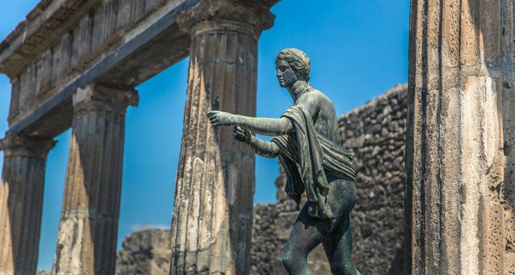 Bronzen standbeeld van Apollo tussen oude zuilen onder een helderblauwe hemel in Pompeii