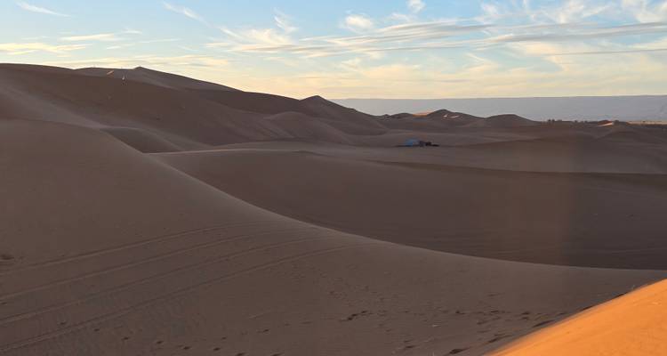 Rolling desert dunes stretch toward the horizon, bathed in warm evening light.