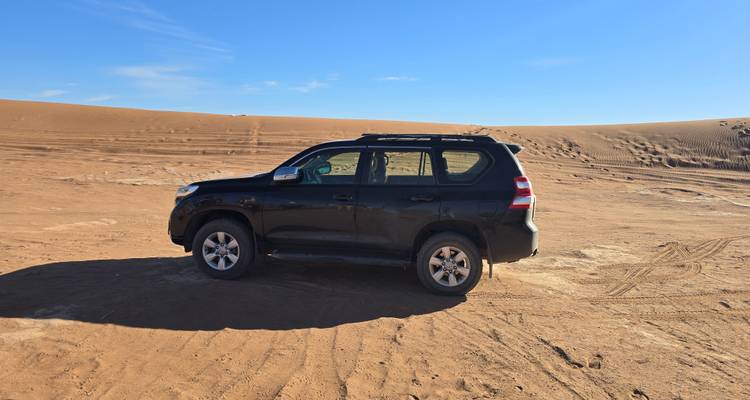 A black 4x4 vehicle parked on an open sandy expanse under a clear blue sky.
