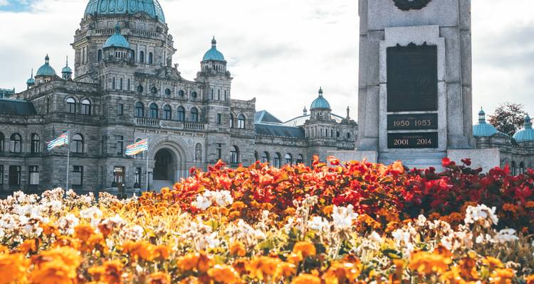Parliament building domes rise behind a bed of vivid orange and red flowers on a bright day.