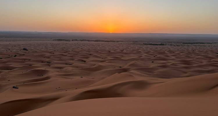 Vast sea of undulating desert dunes glowing orange at sunrise with the sun just above the horizon.