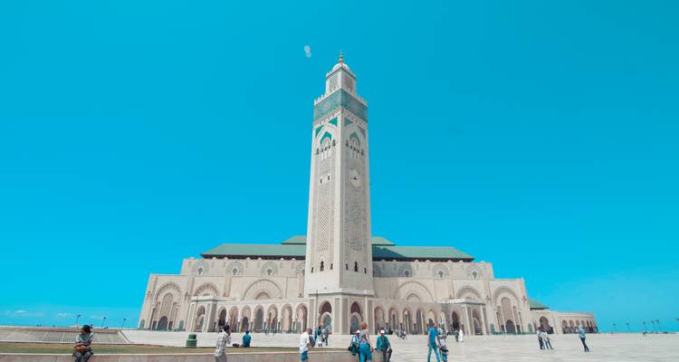 Visitors walk across the vast forecourt in front of Hassan II Mosque under a clear cyan sky.