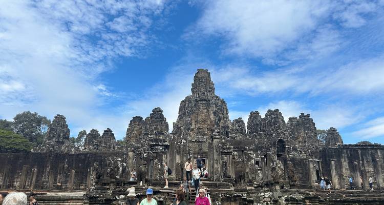 Besucher erkunden den vieltuermigen Bayon-Tempel unter einem strahlend blauen Himmel