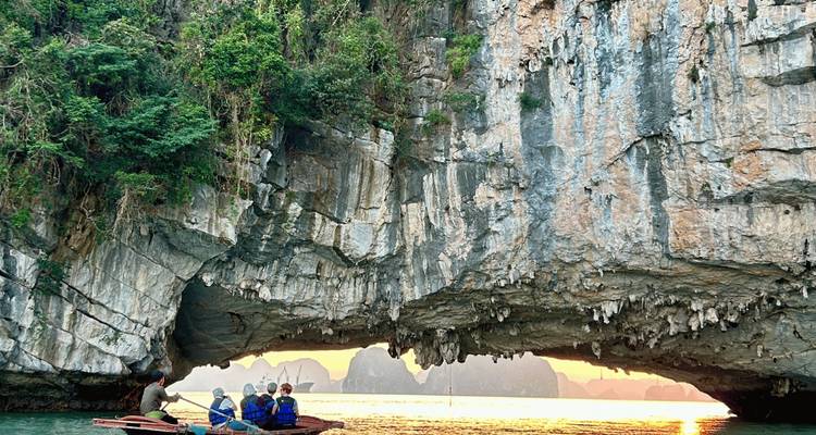 Traditionelles Boot fährt bei Sonnenuntergang unter dramatischem Kalksteinfelsen in der Ha-Long-Bucht
