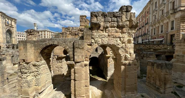 Steinbogen und Mauern eines antiken römischen Amphitheaters vor der Kulisse von Stadtgebäuden