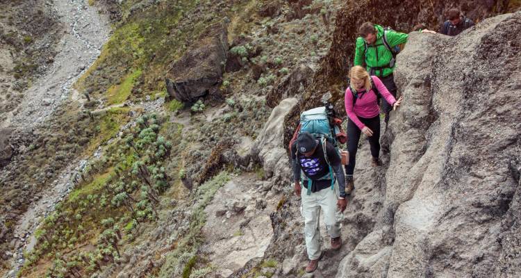 Trekkers in bright gear scramble up a rocky ridge on Mount Kilimanjaro’s trail.