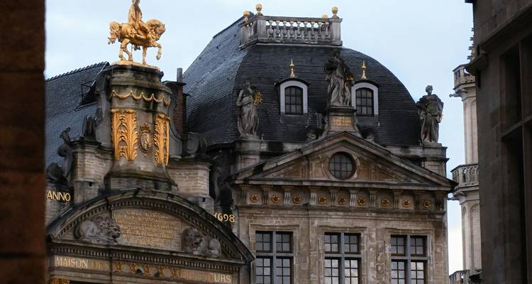 Maison de corporation baroque ornée couronnée d'une statue équestre dorée dans une lumière douce.