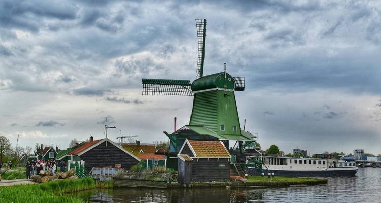 Grand moulin vert à côté d'un canal avec des touristes se promenant le long du sentier sous un ciel nuageux.
