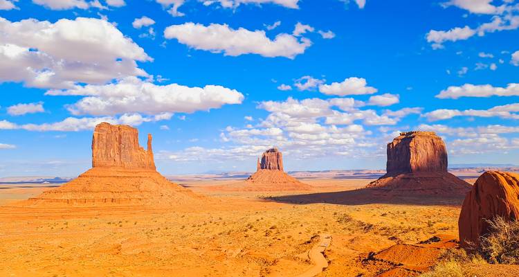Iconic red buttes of Monument Valley rise from the desert under a vivid blue sky.