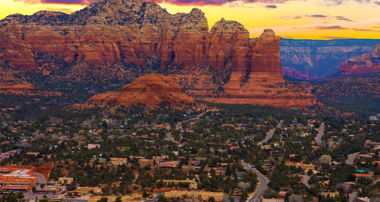 Sedona town sprawls below glowing red rock cliffs at sunset.