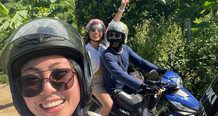 Three friends taking a selfie on motorbikes amid lush tropical countryside.