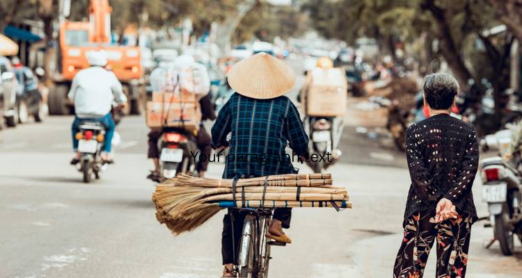 Rear view of cyclist wearing a conical hat carrying bundles on a busy Vietnamese street (text overlay present).