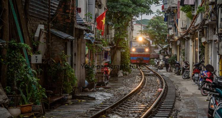 Train approaching along narrow tracks flanked by old houses and motorbikes in Hanoi