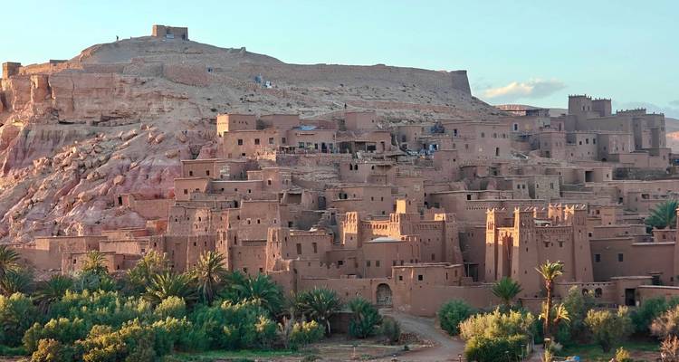 Earthen kasbah village stacked on a hillside at Aït Benhaddou glowing in warm evening light.