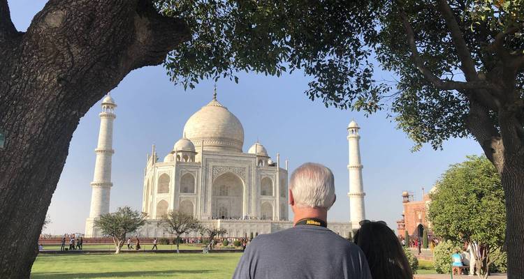A couple admire the Taj Mahal through a tree-framed view on a sunny afternoon.