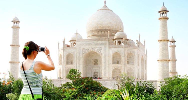 A visitor photographs the Taj Mahal from lush gardens under a clear sky.