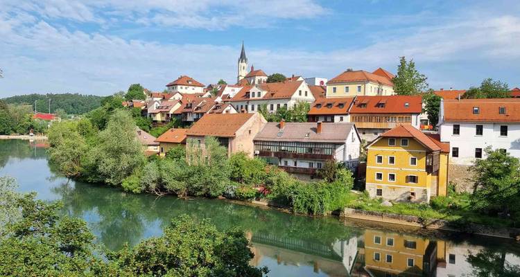 Petite ville pittoresque au bord de la rivière avec des maisons colorées et un clocher d'église se reflétant dans une eau calme.