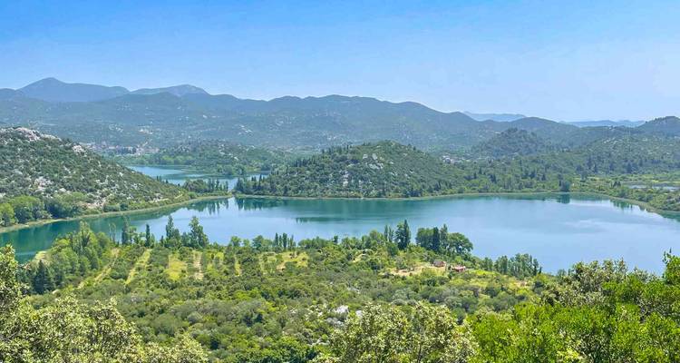 Vue panoramique sur plusieurs lacs émeraude entourés de collines verdoyantes ondulantes et de montagnes lointaines sous un ciel bleu éclatant.