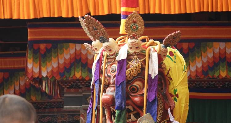 Elaborada máscara de dragón con tela multicolor y rostros tallados exhibida en el escenario de un festival bhutanés.
