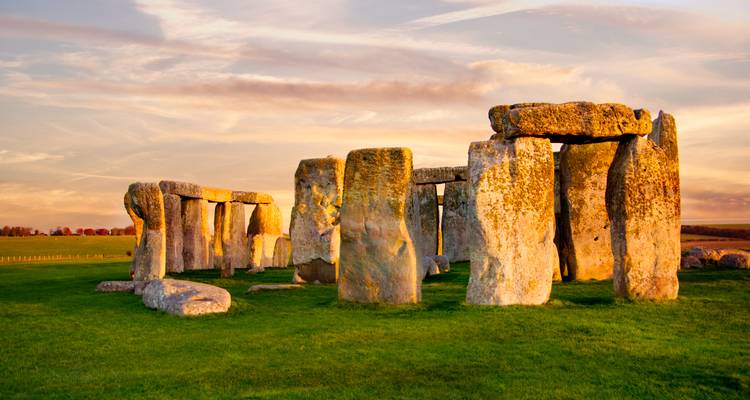Golden sunlight bathes the prehistoric stone circle of Stonehenge on a green plain.