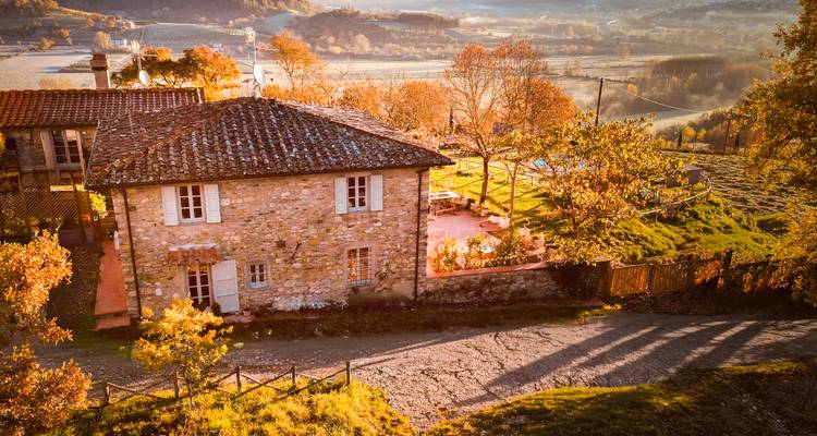 Charming stone farmhouse and autumnal trees bathed in golden hour light overlooking Tuscan countryside.