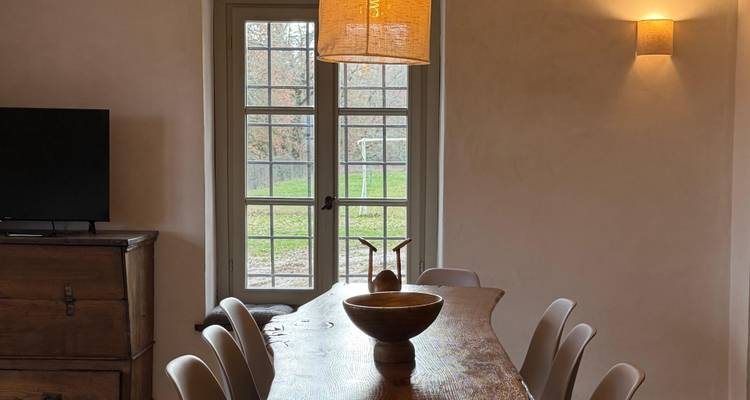 Cozy dining room with long wooden table, modern chairs, pendant lamp and a windowed door to a green yard