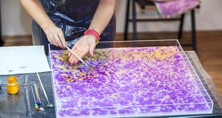 Artist demonstrates traditional Ebru marbling, swirling paints on purple water bath