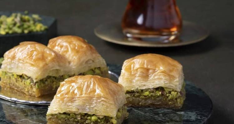 Close-up of flaky pistachio baklava pieces beside a glass of Turkish tea