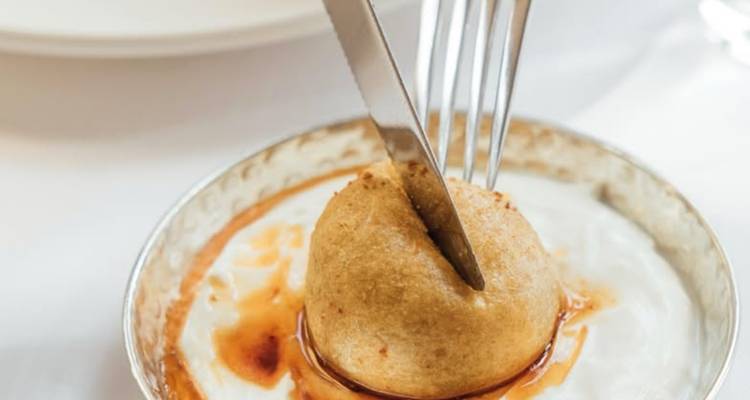 Fork and knife slicing into a syrup-covered Turkish dessert served on yogurt.
