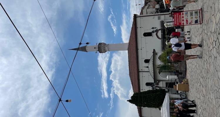 Un alto minarete que se alza sobre una mezquita blanca rodeada de visitantes paseando.