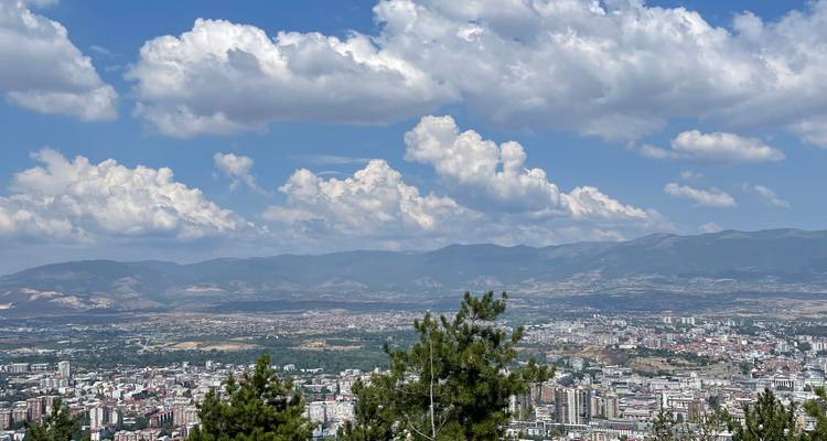 Vista panorámica de la ciudad a vista de pájaro respaldada por cadenas montañosas escarpadas bajo nubes esponjosas.