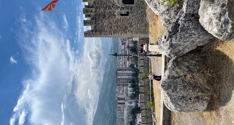 Los muros de piedra de una fortaleza en la cima de la colina dominan la ciudad con una bandera nacional ondulando.