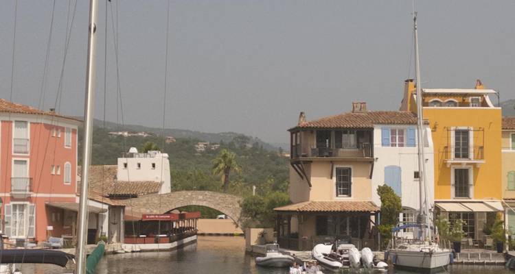 Quiet canal bend with sailboats and colorful Mediterranean houses topped by a stone bridge